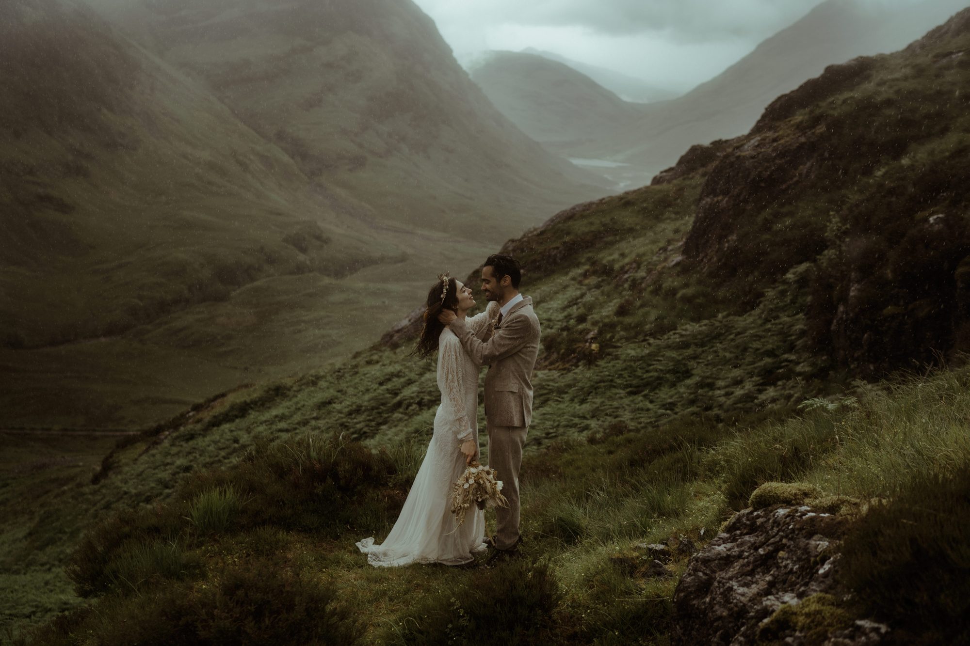 A couple in a wide green valley in Glencoe, bride in white against the mountains